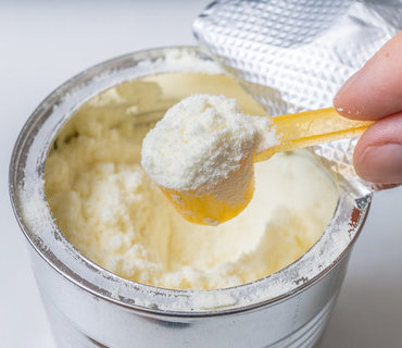 Hand holds scoop with newborn milk formula. Hand holds scoop with newborn milk formula.