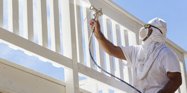 House Painter Wearing Facial Protection Spray Painting A Deck of A Home. House Painter Wearing Facial Protection Spray Painting A Deck of A Home.