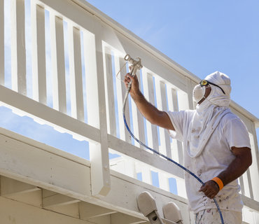 House Painter Wearing Facial Protection Spray Painting A Deck of A Home. House Painter Wearing Facial Protection Spray Painting A Deck of A Home.