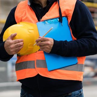 construction worker with orange safety vest holding a yellow helmet